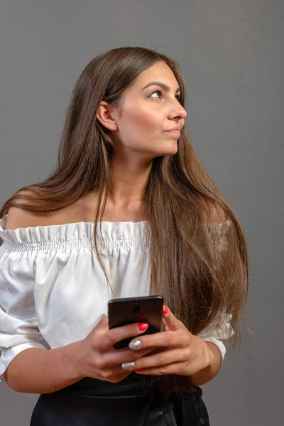 Photo d'une femme souriante aux longs cheveux foncés tenant et utilisant un téléphone portable noir isolé sur fond gris — Photo