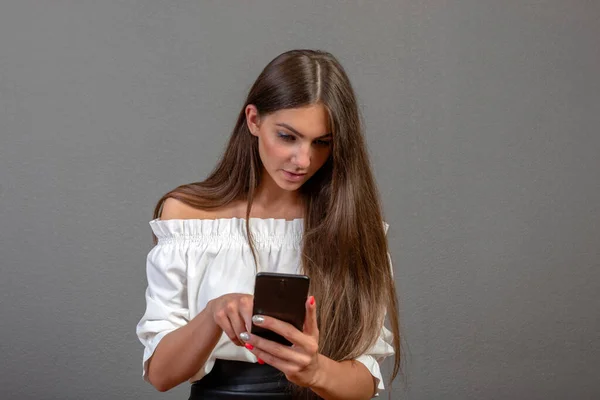 Mujer joven sonriente usando aplicaciones de teléfono celular, atractiva mujer mirando la pantalla del dispositivo móvil, chica charlando en línea en la red social, leyendo buenas noticias, mensaje, aislado en el fondo del estudio — Foto de Stock