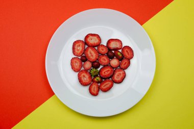 Yaratıcı Sevgililer Günü romantik konsept kompozisyon düz turuncu ve sarı arka plan üzerinde izole beyaz bir tabak üzerinde kalp çilek ile üst görünümü yatıyordu. 