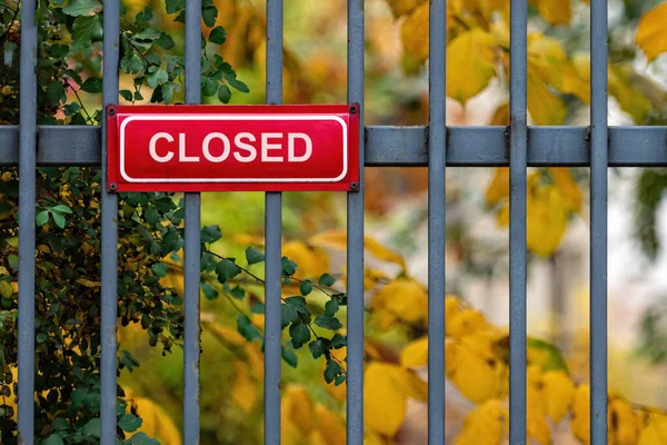 red metal sign with an inscription CLOSED on a decorative metal fence, defocused autumn trees in background
