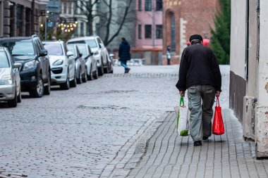 Eski kasabanın asfalt sokakları boyunca çantalı yaşlı adam gider. Arka görünüm