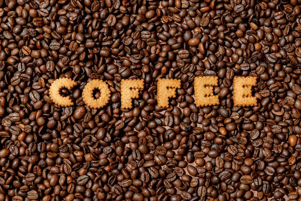 A palavra COFFEE feita de letras de biscoito em um fundo de grão de café escuro — Fotografia de Stock