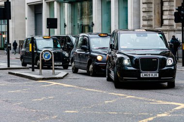 London, England, UK - December 31, 2019:   Typical black London cab in city streets. Traditionally Taxi cabs are all black in London but now produced in various colors clipart