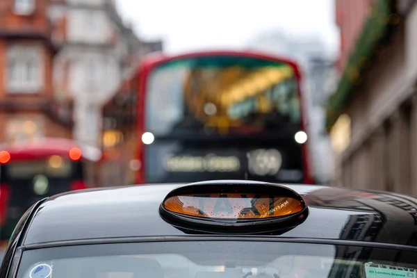Лондон, Англия, Великобритания - 31 декабря 2019 г.: Британское чёрное такси с разряженным красным автобусом на заднем плане — стоковое фото