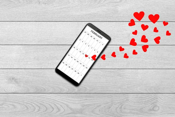 Conceito de dia dos namorados, mensagem de amor corações voando para fora smartphone, isolado no fundo de madeira branca, calendário no smartphone — Fotografia de Stock