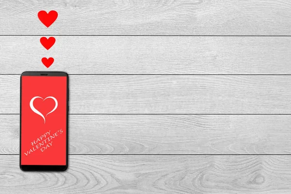 Концепція дня Святого Валентина, любовне повідомлення - серця, що вилітають зі смартфона, ізольовані на білому дерев'яному фоні — стокове фото