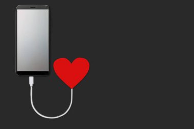 Aşkın gücü kavramı, karanlık arka planda izole edilmiş cep telefonu ile kırmızı kalpten şarj olan boş ekran, düz yatar