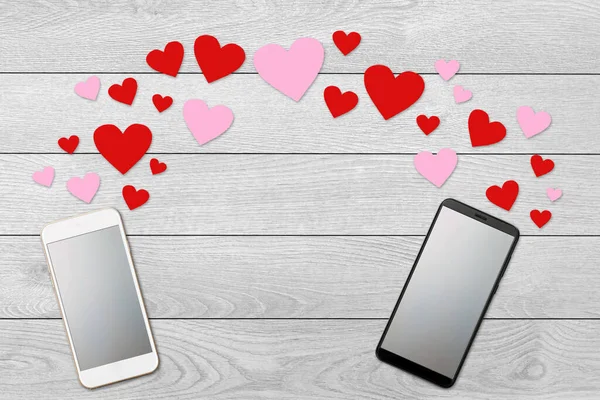Conceito de dia dos namorados, mensagem de amor corações voando para fora de dois smartphones, Isolado em fundo de madeira branca, flat lay — Fotografia de Stock