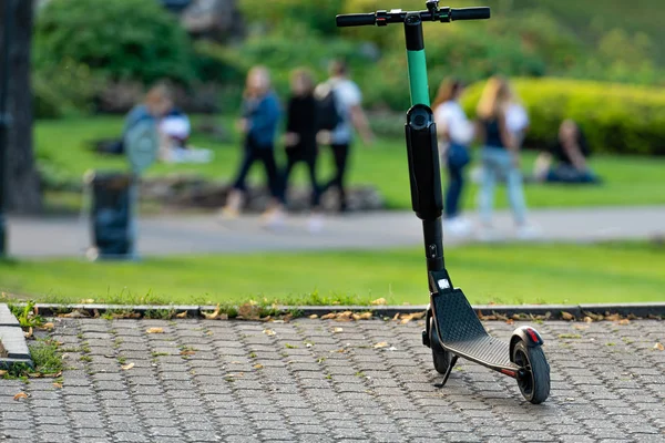 Scooter elétrico ou e-scooter estacionado na calçada, fundo do parque borrado - imagem — Fotografia de Stock