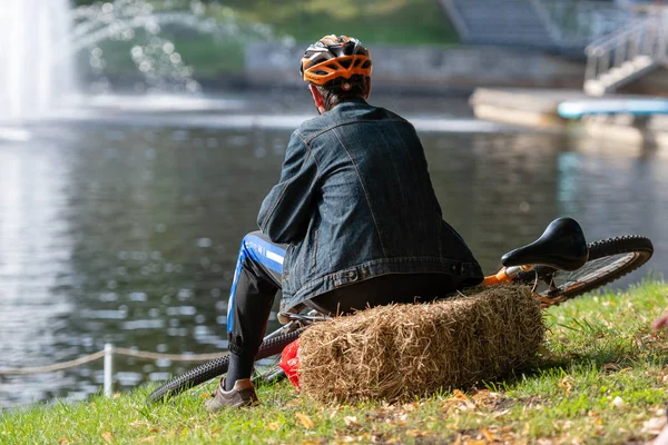 Riga, Latvia - August 16, 2019: a cyclist sits on a straw bale in a city park by the canal and relaxes — 스톡 사진