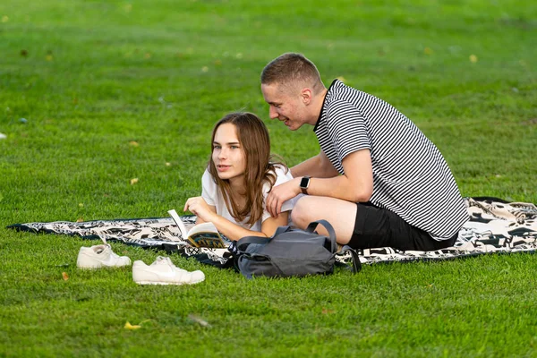 Riga, Latvia - August 16, 2019: a couple of young people are resting on the park lawn and reading a book — Stock Photo, Image