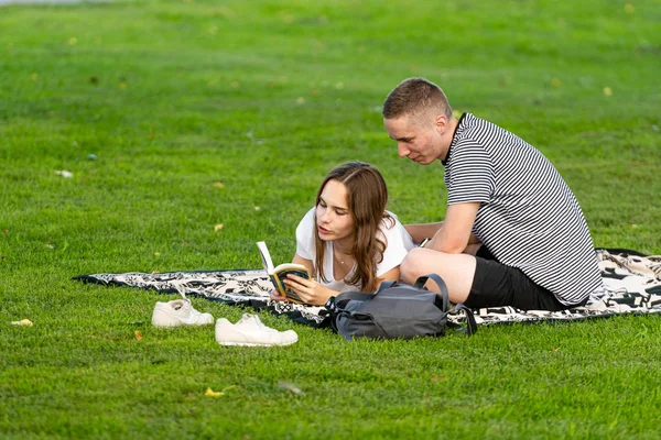 Riga, Latvia - August 16, 2019: a couple of young people are resting on the park lawn and reading a book — Stock Photo, Image