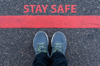man in sneakers standing next to a red line with text STAY SAFE, restriction or safety warning concept clipart