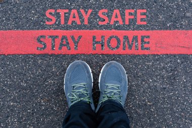 man in sneakers standing next to a red line with text STAY SAFE, STAY HOME, restriction or safety warning concept clipart