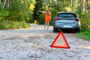 Stresli genç kadın sürücü otostop çeker ve arabaları durdurur, bozuk arabalarla ilgili sorun olduğu için yardım ister, sürücüleri durdurmak için kırmızı üçgen işareti kullanır. (seçici odaklanma)