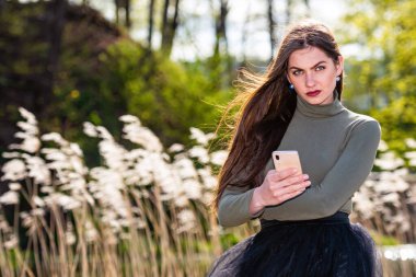 Güneşli ve rüzgarlı bir günde güzel, duygusal esmer bir kadın akıllı telefondaki mesajı okuduğunda üzülür.