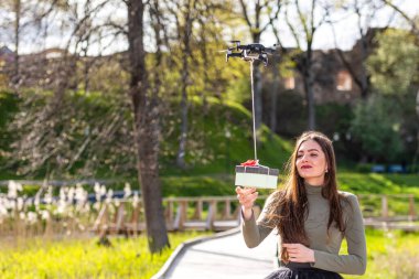 Güneşli ve rüzgarlı bir günde gülümseyen duygusal esmer kuadkopter, insansız hava aracı teslimat hizmeti ve modern hızlı dağıtım metodu konseptiyle sürpriz bir hediye alır.