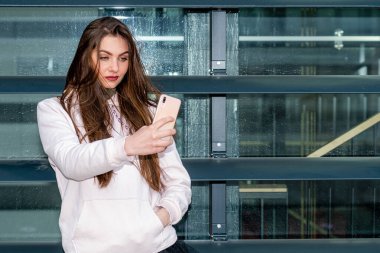 Genç duygusal esmer kadın akıllı telefon kullanıyor. Şehirli bir arka planda selfie çekiyor.