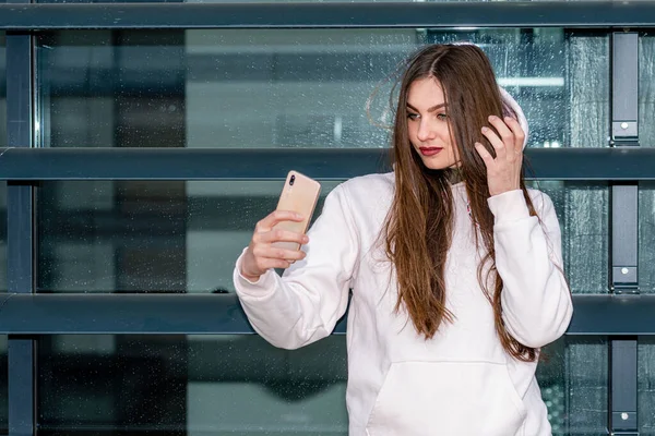 Genç duygusal esmer kadın akıllı telefon kullanıyor. Şehirli bir arka planda selfie çekiyor.