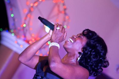 Güzel Afrikalı şarkıcı kadın mikrofonuyla arka planda renkli ışıklar eşliğinde şarkı söylüyor.