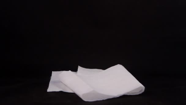 Крупным планом использованного женского гигиенического тампакса, который хранится на белой оригинальной бумаге с голубыми медицинскими перчатками на черном фоне — стоковое видео