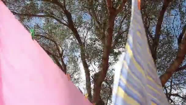Giù vista da vicino di vestiti con lenzuola colorate appese al filo con mollette colorate per appendere il bucato svolazzante al vento — Video Stock