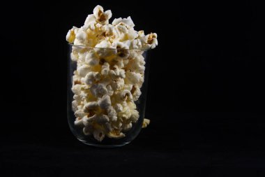 Hareket etmeyi kes şeffaf bir bardağı dolduran çıtır çıtır patlamış mısırı kapat ve siyah arka planda çık.