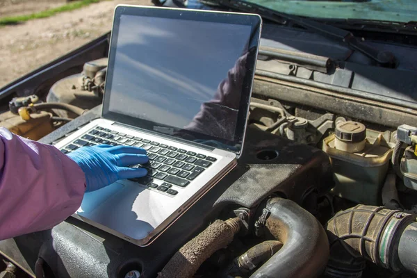 オープンラップトップの近くにディーゼルエンジンのオイルを交換し 充填する準備をしている整備士の手 — ストック写真