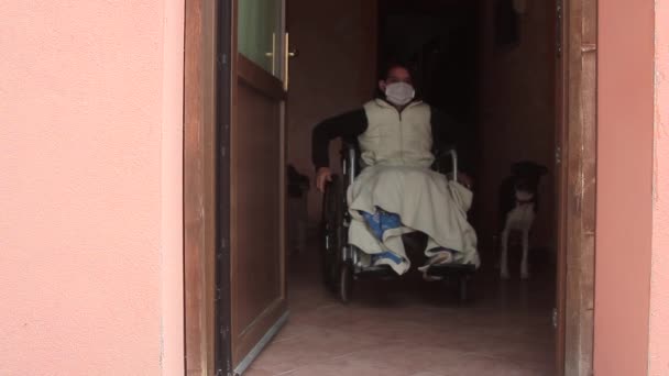 Femme handicapée seule dans un fauteuil roulant avec un masque de protection regardant par la porte des portes ouvertes rester à la maison pour la quarantaine — Video