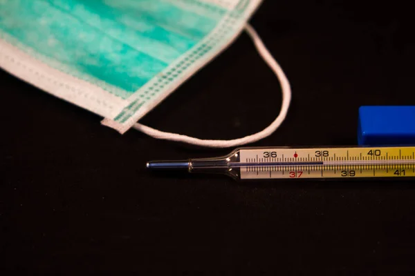 close up of mercury thermometer indicating high fever with green healthcare mask and blue medical glove fingers