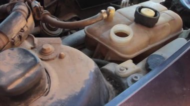 Mavi eldivenli bir tamircinin eli dizel bir arabanın motorunun radyatörünün su deposunu dolduruyor.