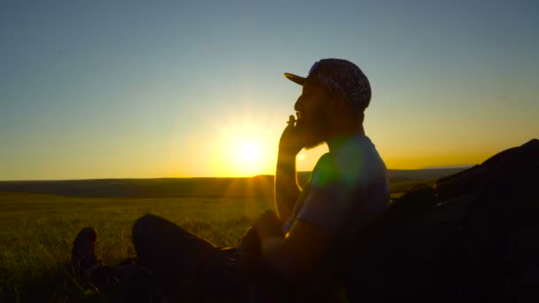 Silhouette d'un randonneur barbu qui fume une cigarette roulée au coucher du soleil — Video