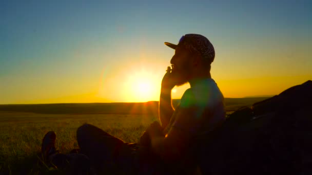 Silhouette di un escursionista barbuto che fuma sigarette roll-up al tramonto — Video Stock