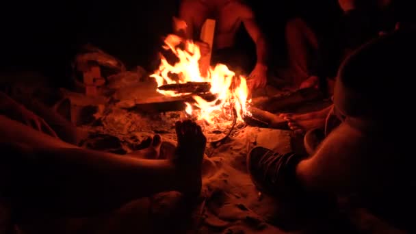 Groupe d'amis assis près de feu de camp à la plage de l'océan de nuit et traîner. 4K UHD  .