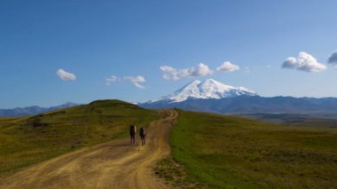 İki adam Kafkasya dağlarında karayoluyla hiking. Arkadaşlar Elbruz Dağı geniş sahne 4k gidiyor Uhd
