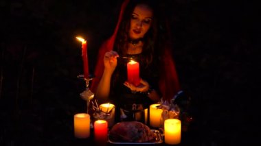 Kırmızı pelerin içinde mum ile çekici güzel esmer cadı mistik sonbahar ormanda çağrıştırıyor. büyücülük bir kalp, tavuk budu ve kirpi iğne ile