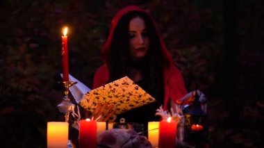 Kırmızı pelerin içinde çekici güzel esmer cadı mistik sonbahar ormanda çağrıştırıyor. büyücülük bir kalp, tavuk budu ve kirpi iğne ile