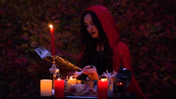 Atraktivní nádherná bruneta čarodějnice v červený plášť, který vyvolává v mystické podzimním lese. čarodějnictví se srdcem, kuřecí stehna a Dikobraz jehly