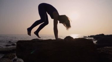 Genç kadın pratik yoga sahilde deniz üzerinde şaşırtıcı güneş doğarken giyerlerdi. Fitness, spor, yoga ve sağlıklı yaşam konsepti. Amut yapıyor kız