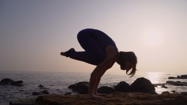 Fiatal nő Body gyakorló jóga a tengerparton a tenger felett, a csodálatos napfelkeltét. Fitness, sport, jóga és egészséges életmód fogalma. Lány csinál a kézen — Stock videók