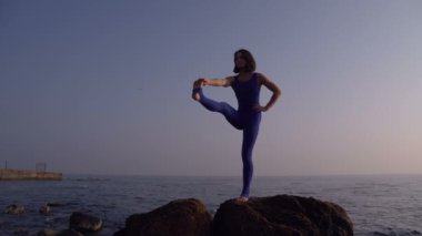 Genç kadın pratik yoga sahilde deniz üzerinde şaşırtıcı güneş doğarken giyerlerdi. Fitness, spor, yoga ve sağlıklı yaşam konsepti. Tek bacak yapıyor kız ayağa ve sicim