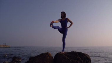 Genç kadın pratik yoga sahilde deniz üzerinde şaşırtıcı güneş doğarken giyerlerdi. Fitness, spor, yoga ve sağlıklı yaşam konsepti. Tek bacak yapıyor kız ayağa ve sicim