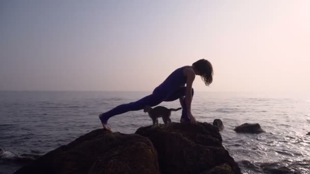 Jovem mulher em bodysuit praticando ioga na praia acima do mar ao nascer do sol incrível. Fitness, esporte, ioga e conceito de estilo de vida saudável. Menina fazendo complicado ioga asana — Vídeo de Stock