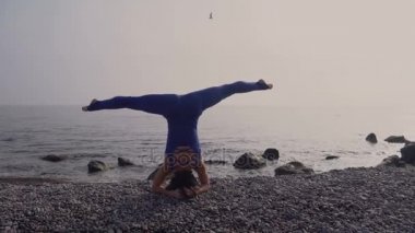 Genç kadın pratik yoga sahilde deniz üzerinde şaşırtıcı güneş doğarken giyerlerdi. Fitness, spor, yoga ve sağlıklı yaşam konsepti. Kız işi kafasına stand ve sicim