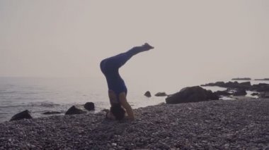 Genç kadın pratik yoga sahilde deniz üzerinde şaşırtıcı güneş doğarken giyerlerdi. Fitness, spor, yoga ve sağlıklı yaşam konsepti. Kız işi kafasına stand ve sicim
