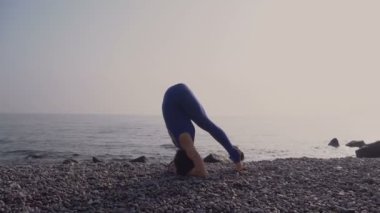 Genç kadın pratik yoga sahilde deniz üzerinde şaşırtıcı güneş doğarken giyerlerdi. Fitness, spor, yoga ve sağlıklı yaşam konsepti. Kız işi kafasına stand ve sicim