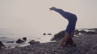 Genç kadın pratik yoga sahilde deniz üzerinde şaşırtıcı güneş doğarken giyerlerdi. Fitness, spor, yoga ve sağlıklı yaşam konsepti. Karmaşık yoga asana yaparken kız