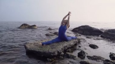 Genç kadın pratik yoga sahilde deniz üzerinde şaşırtıcı güneş doğarken giyerlerdi. Fitness, spor, yoga ve sağlıklı yaşam konsepti. Karmaşık yoga asana yaparken kız