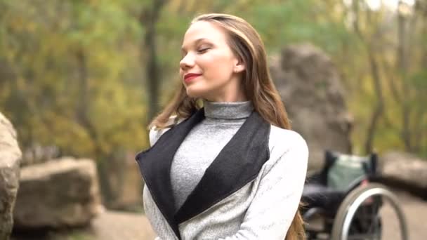 Attractive girl on a wheelchair sitting on stone in the autumn park. Disabled leisure — Stock Video