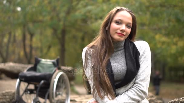 Menina atraente em uma cadeira de rodas sentada em pedra no parque de outono. Lazer deficiente — Vídeo de Stock